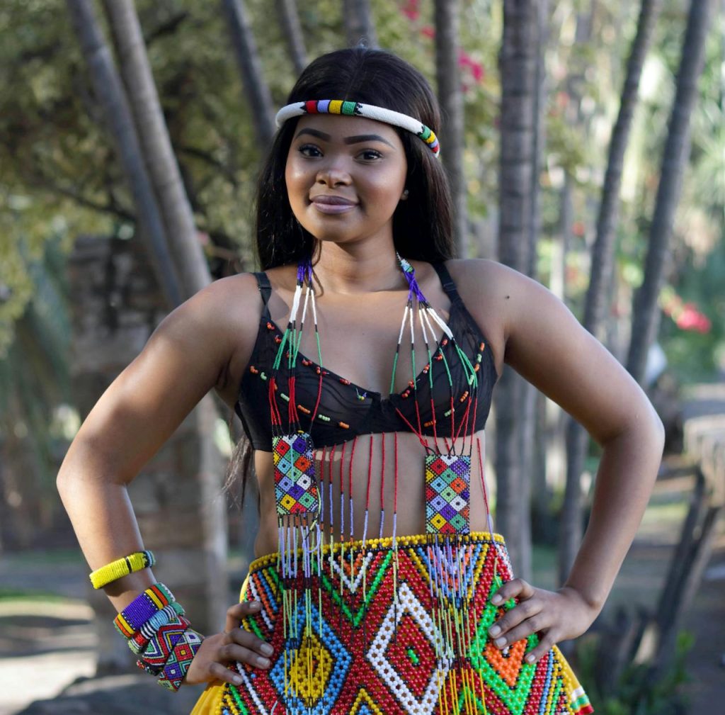 Young woman in vibrant Zulu attire posing outdoors with a confident smile.